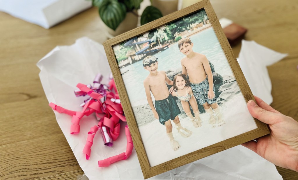 hand holding picture frame with photo of three kids at pool