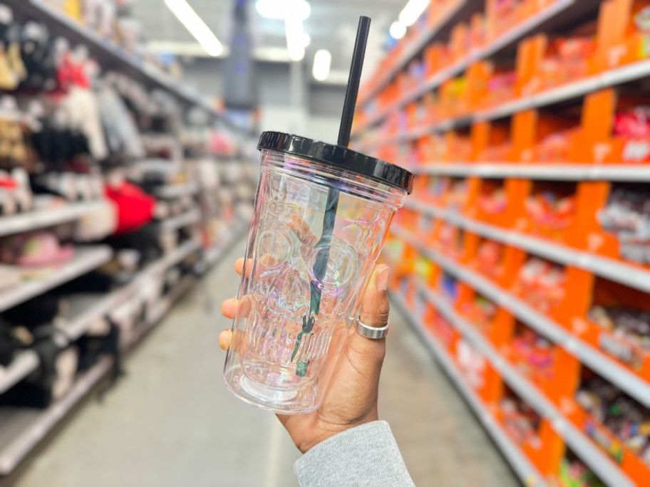 hand holding a glass tumbler with a skull design, black lid and straw