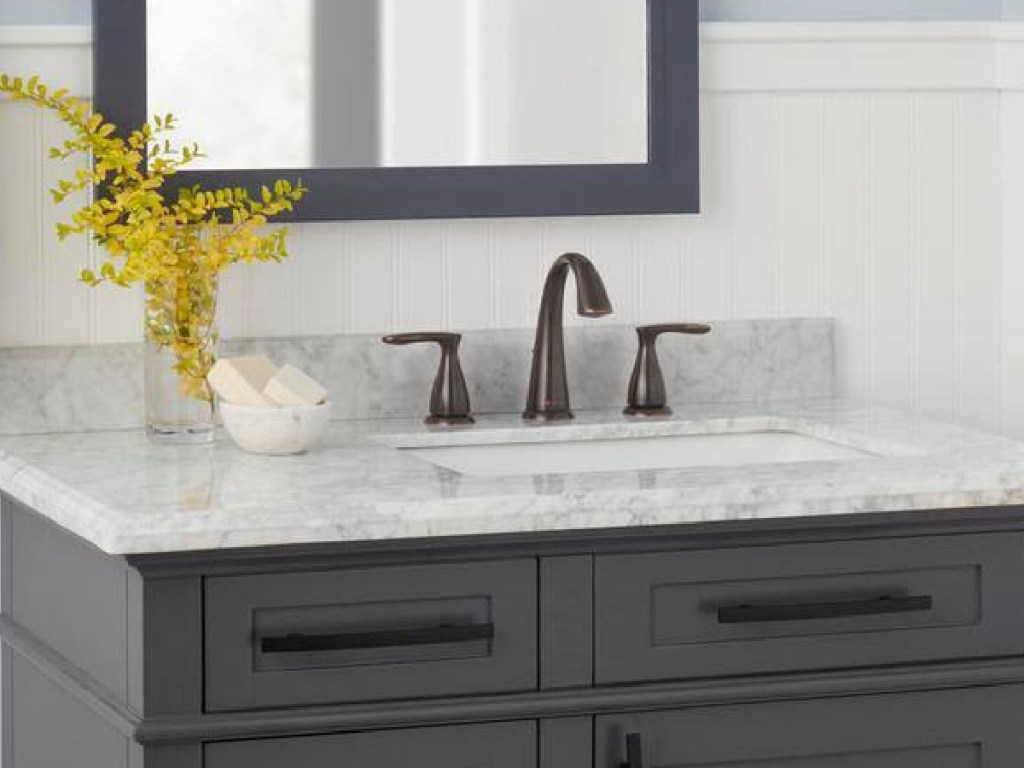 2 handle bathroom faucet in bronze displayed on vanity with flowers to the side of it