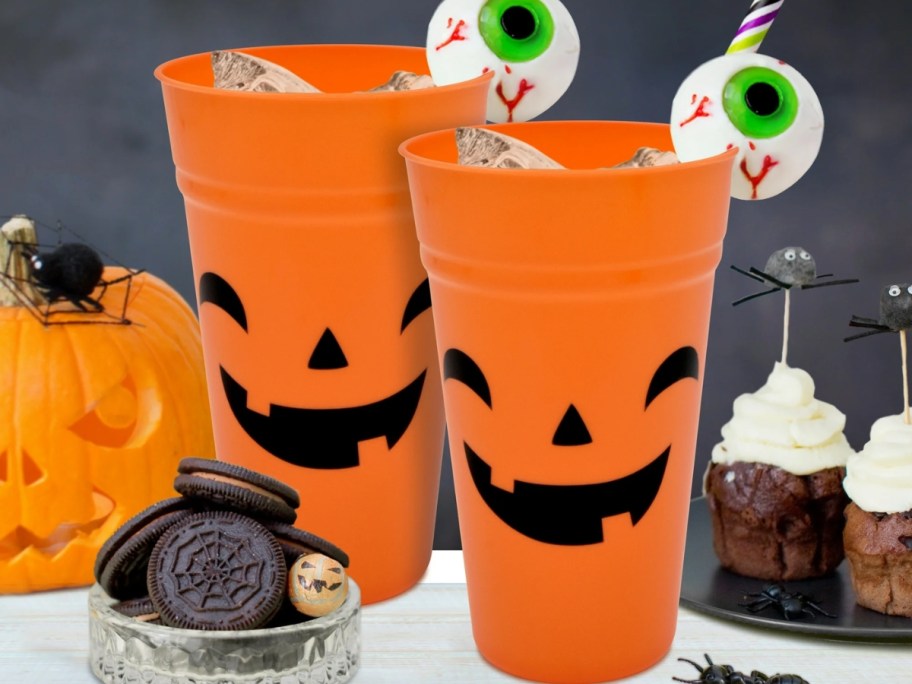 2 orange Jackolantern tumblers with Halloween food and decor around them