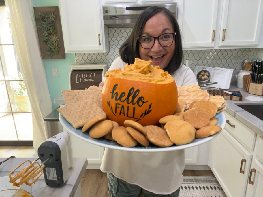 woman holding a fall appetizer of pumpkin pie dip served in a mini pumpkin