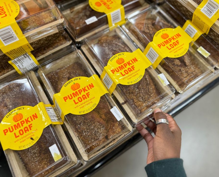 a womans hand grabbing a pumpkin loaf from a store shelf