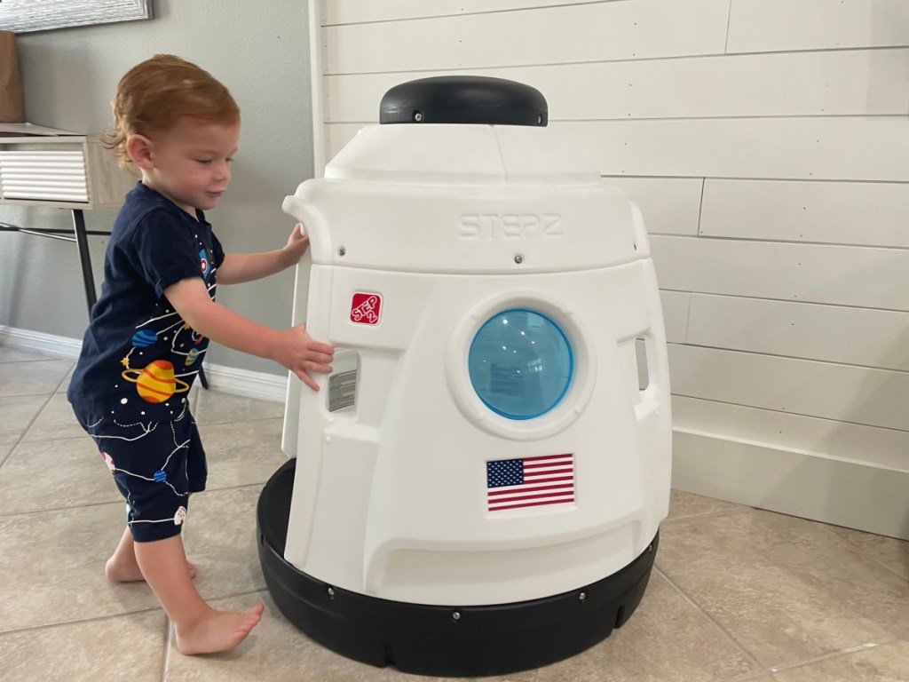 toddler standing next to rocket ship playhouse 