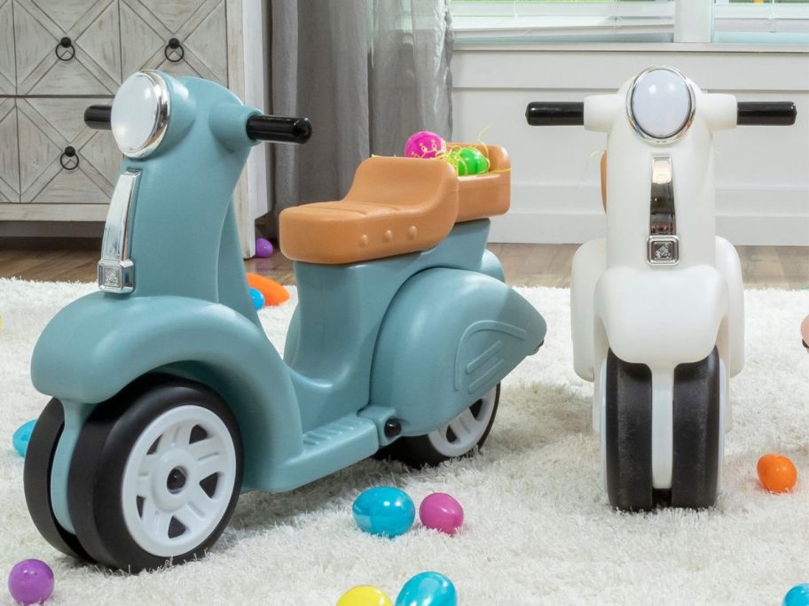 an aqua and white Step2 toddler scooter on a white rug with colorful balls