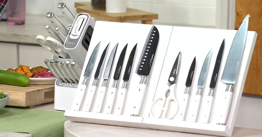 a set of kitchen knives on a white display board with the knife block to the side on a table