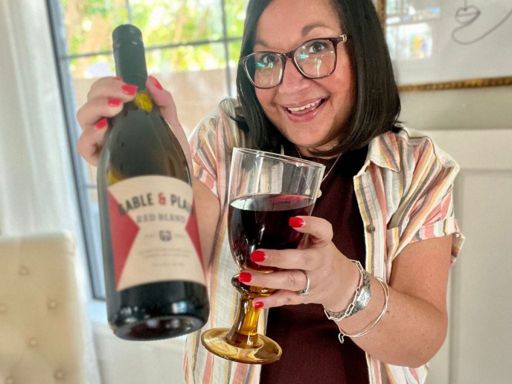 Lina holding up a glass of wine and bottle of wine from Swirl Wine