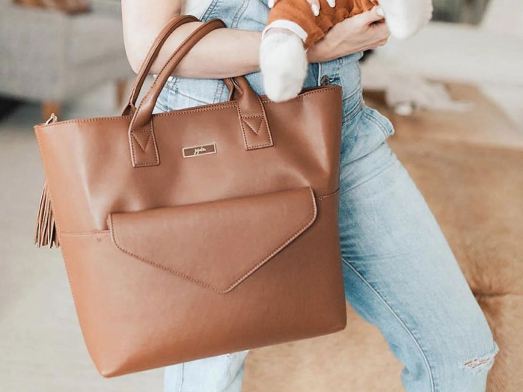 A mom with a baby holding a brown 24-7 TOTE from JuJuBe