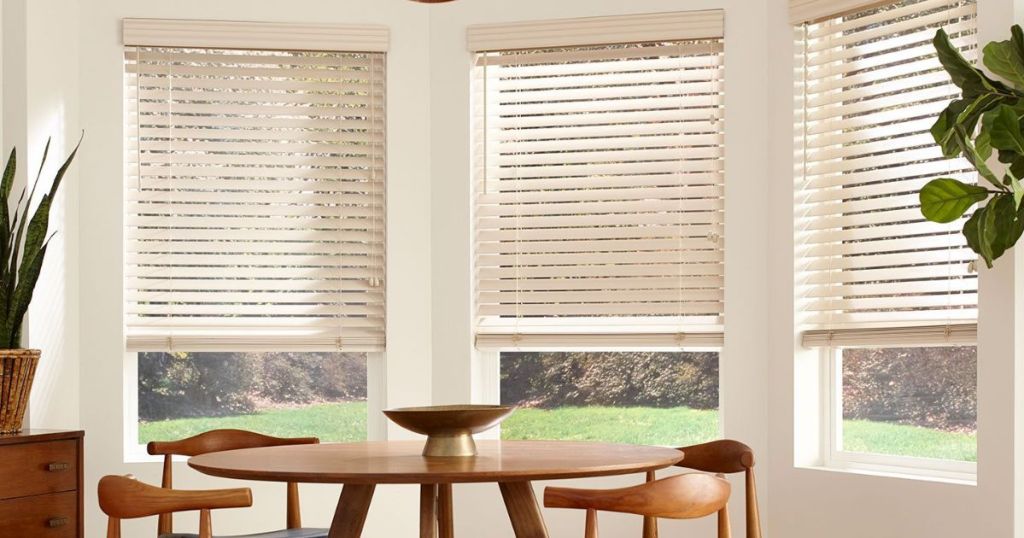 Dining room table surrounded by windows with blinds on them