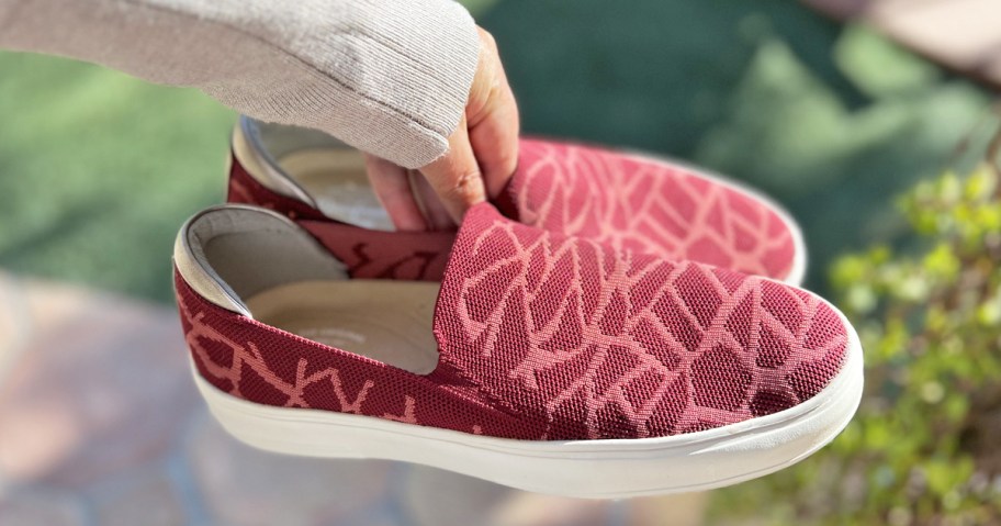 woman holding a pair of red slip-on sneakers
