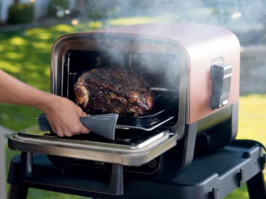 person taking roast out of Ninja Woodfire Outdoor Oven