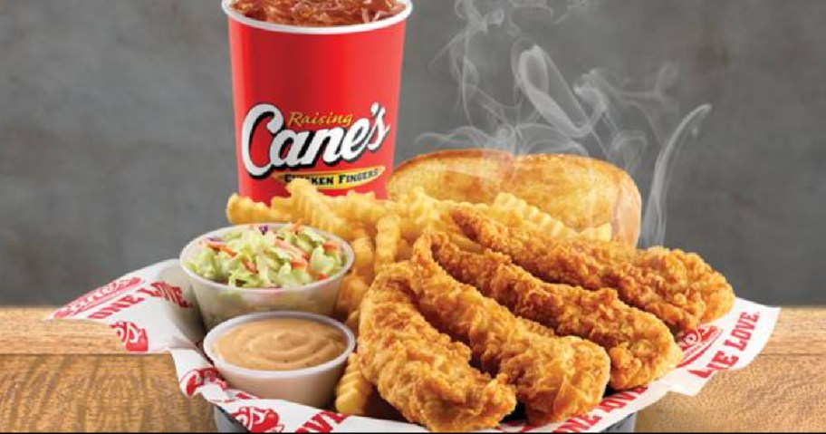 a plate of chicken fingers, fries, slaw, and dipping sauce with a Cane's cup with soda behind it