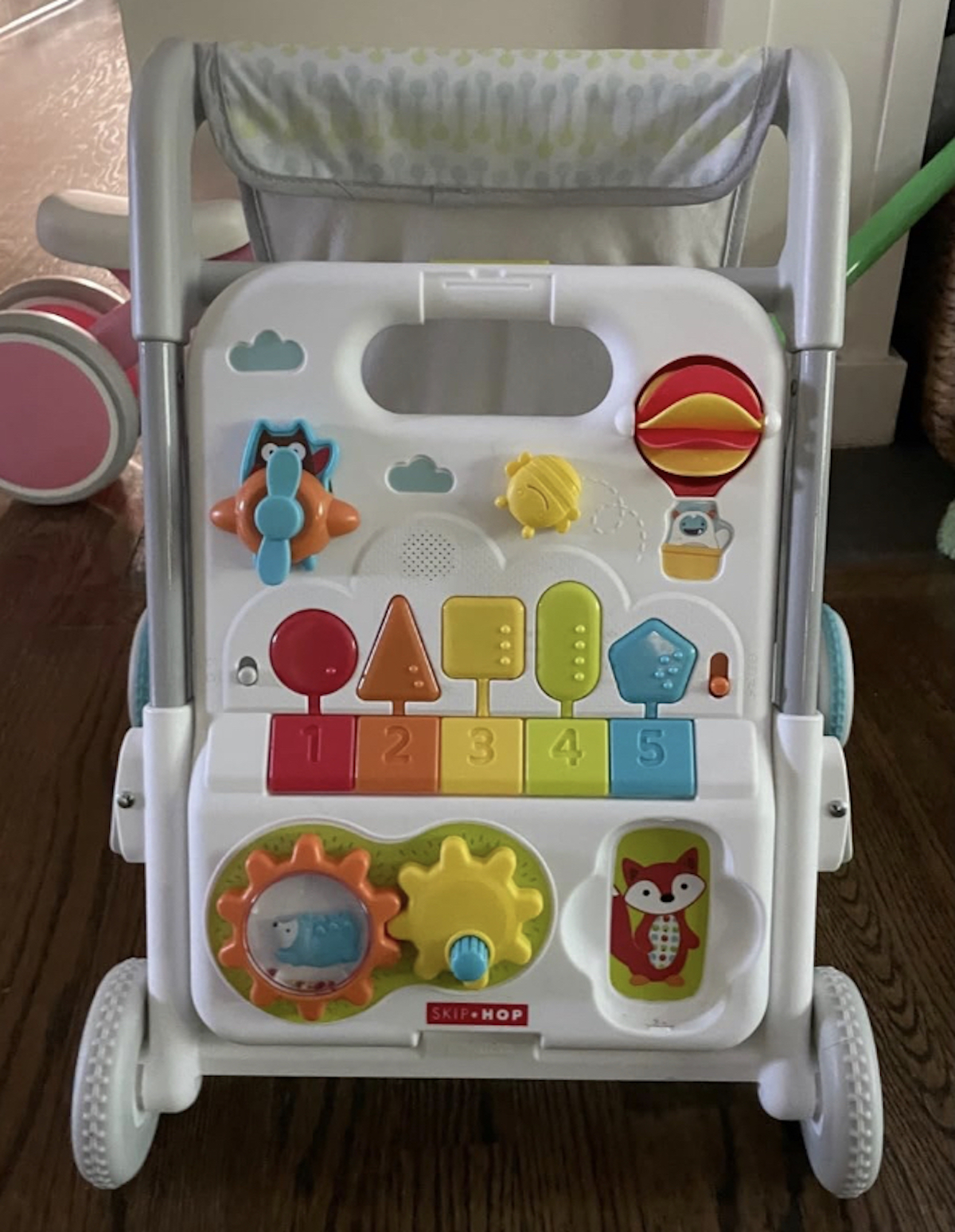 close up of white baby walker with rainbow colored buttons and toys on front