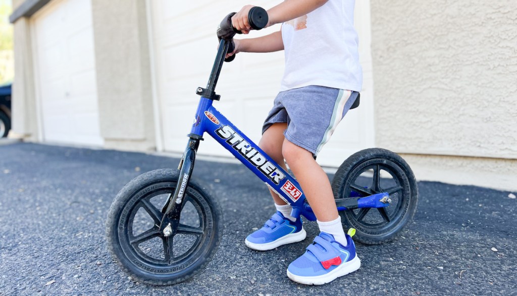 Young kid sitting on blue strider bike in driveway