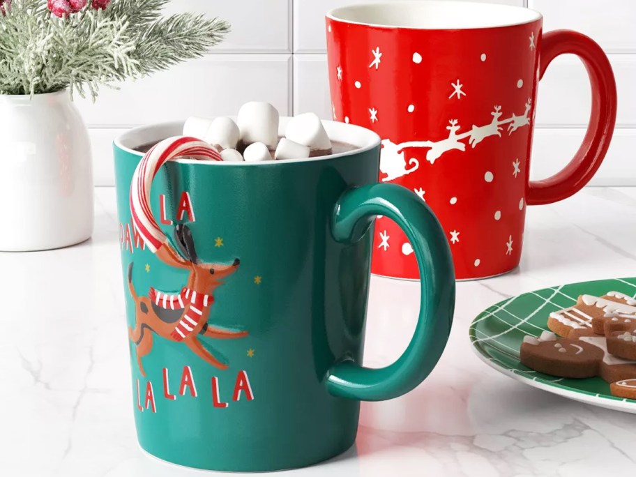 christmas mug with dog that says "Paw La la la" and red mug with santa's sleigh and reindeer