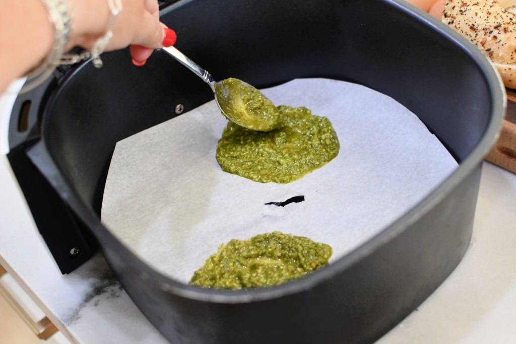 adding pesto to parchment paper inside an air fryer