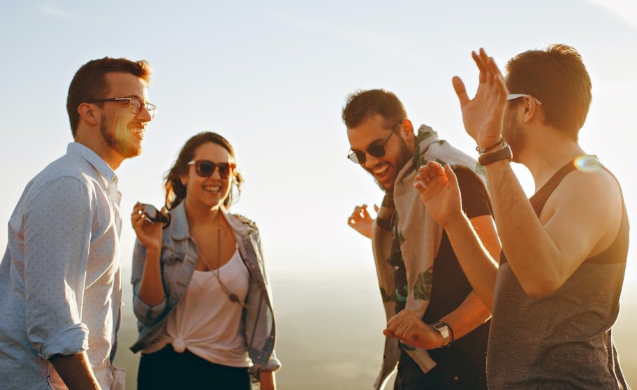 Three adults and woman standing outside in sunshine with sunglasses laughing