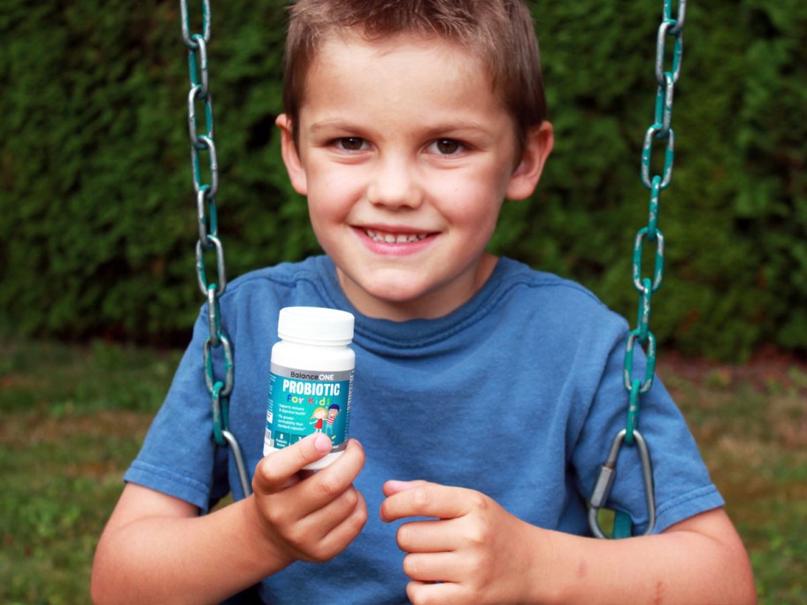 boy on swing in blue shirt holding probiotic bottle