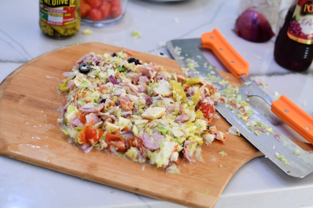 chopped lettuce and veggies with delli meats and cheese on a cutting board