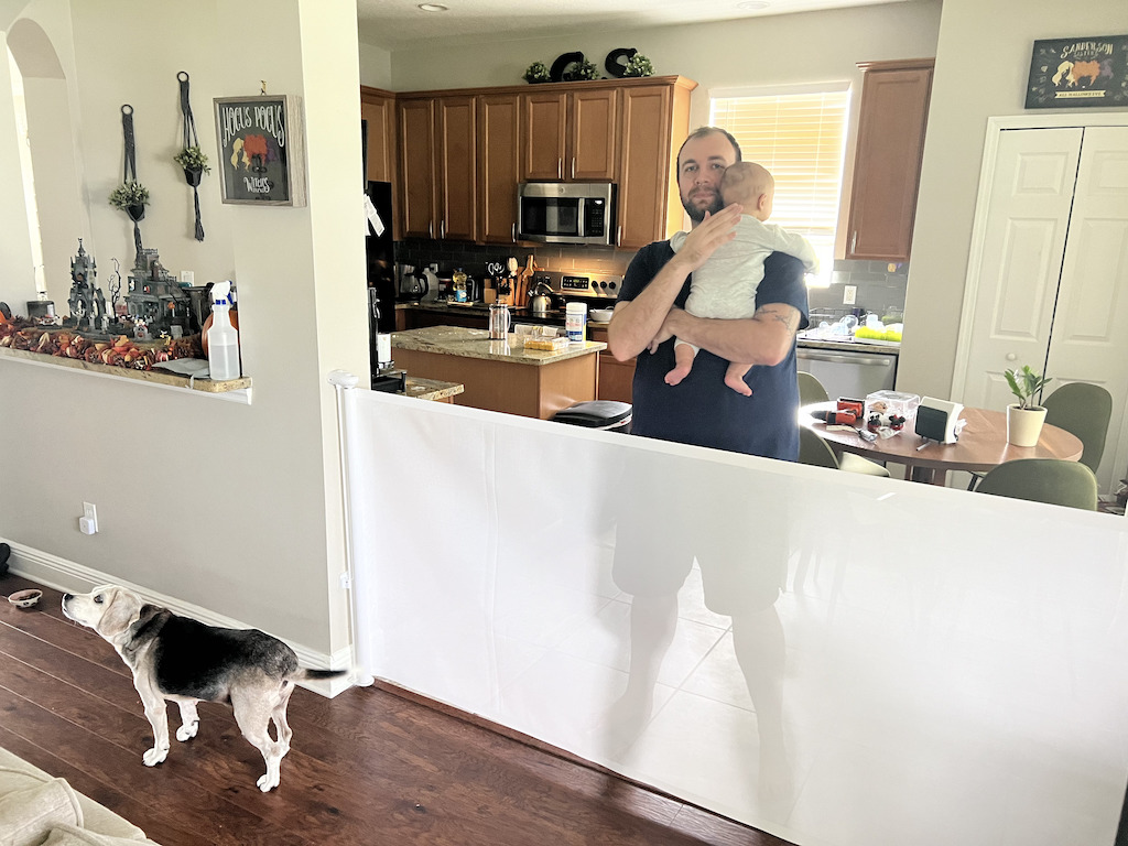 man with baby behind retractible pet gate 