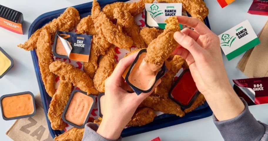 person dipping chicken finger into zaxby's sauce container