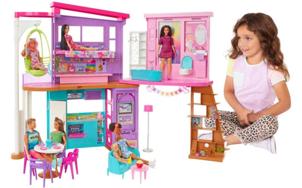 little girl sitting next to a Barbie Vacation House Playset