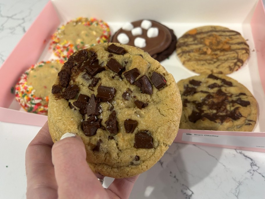 woman holding chocolate chip cookie from crumbl 6 pack