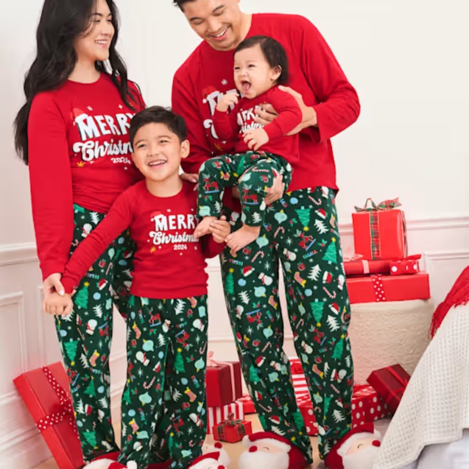 family with mom dad, little boy and baby wearing matching red and green Christmas pajamas that say "Merry Christmas"