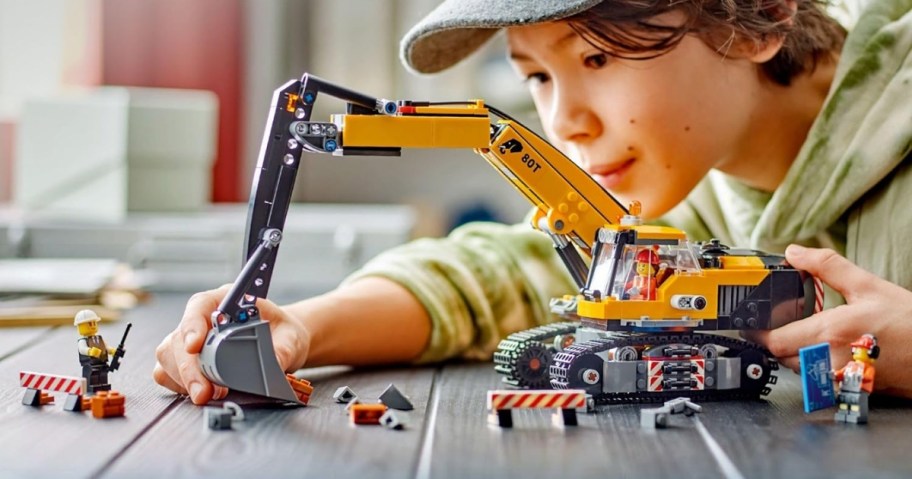 little boy playing with a LEGO set with mini figures and a large yellow and gray Excavator construction vehicle