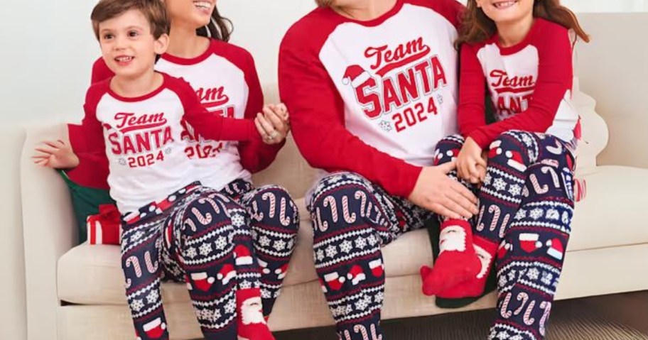 family sitting on a couch wearing matching blue, red and white Christmas pajamas that say "Team Santa"