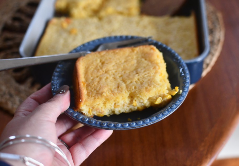 hand holding a plate with a slice of cornbread casserole