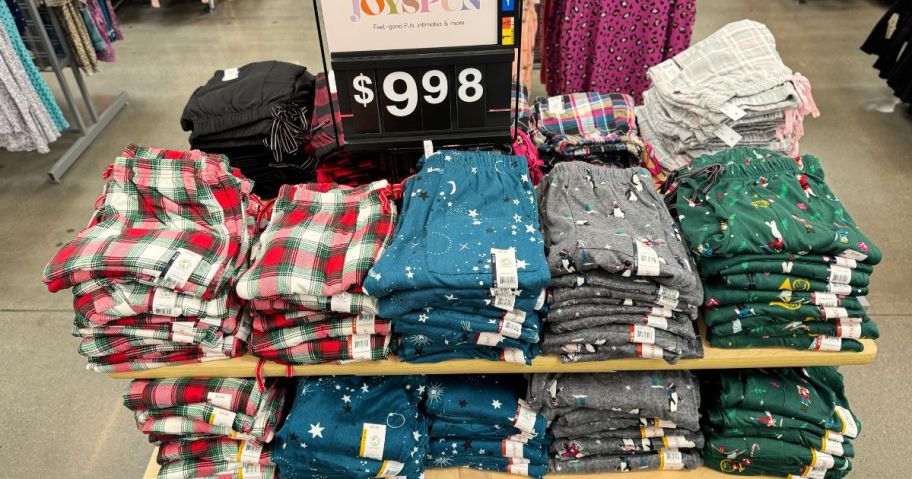 several pairs in different colors and prints of JoySpun Christmas pajama pants on a display table in Walmart