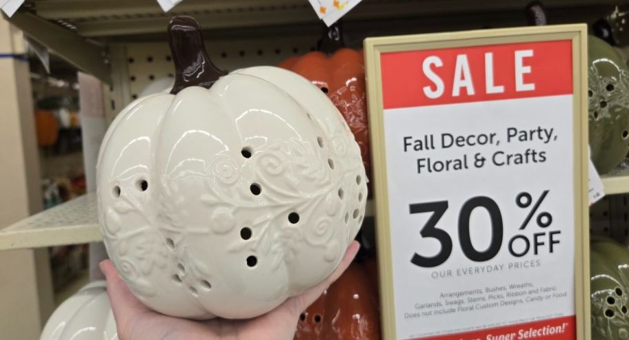 hand holding white light up pumpkin with 30% off discount displayed on the wall