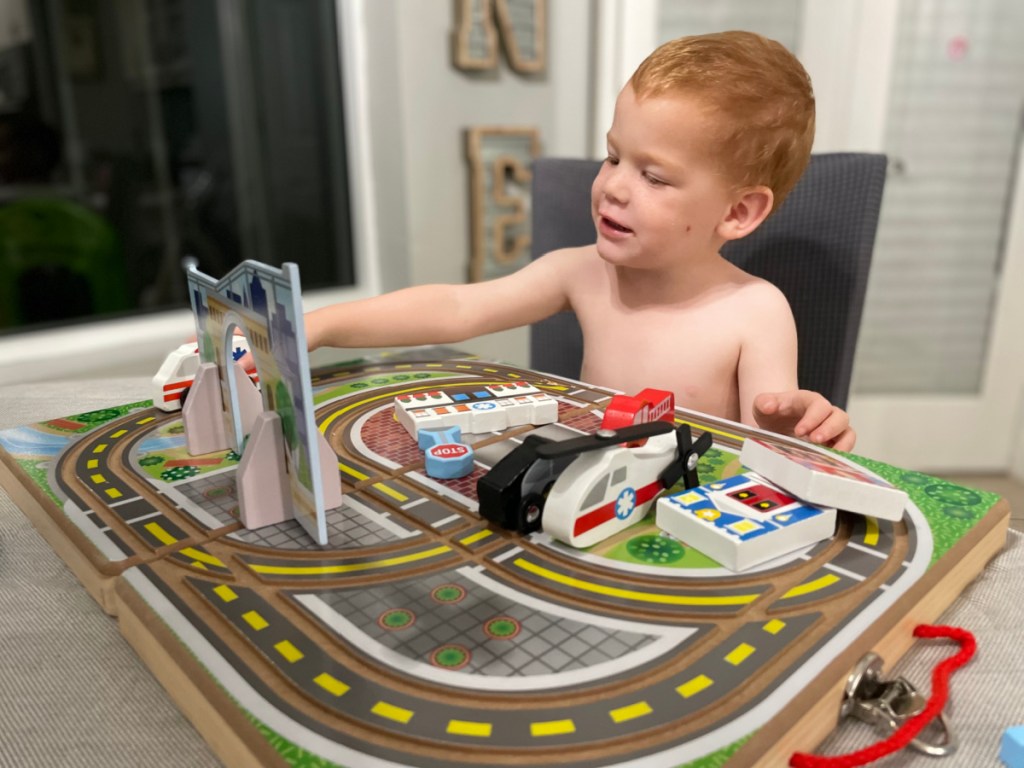 A boy playing with the Melissa and Doug Wooden Take Along Tabletop Town