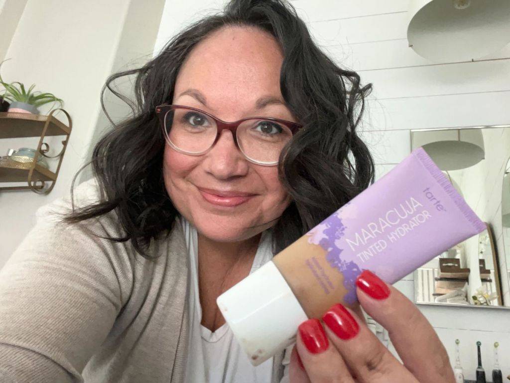 A woman holding a tube of Tarte Maracuja Tinted Hydrator 