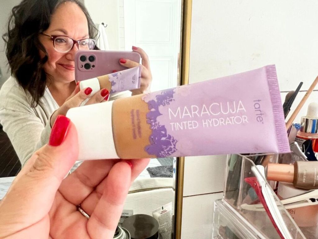 A woman holding a tube of Tarte Maracuja Tinted Hydrator 