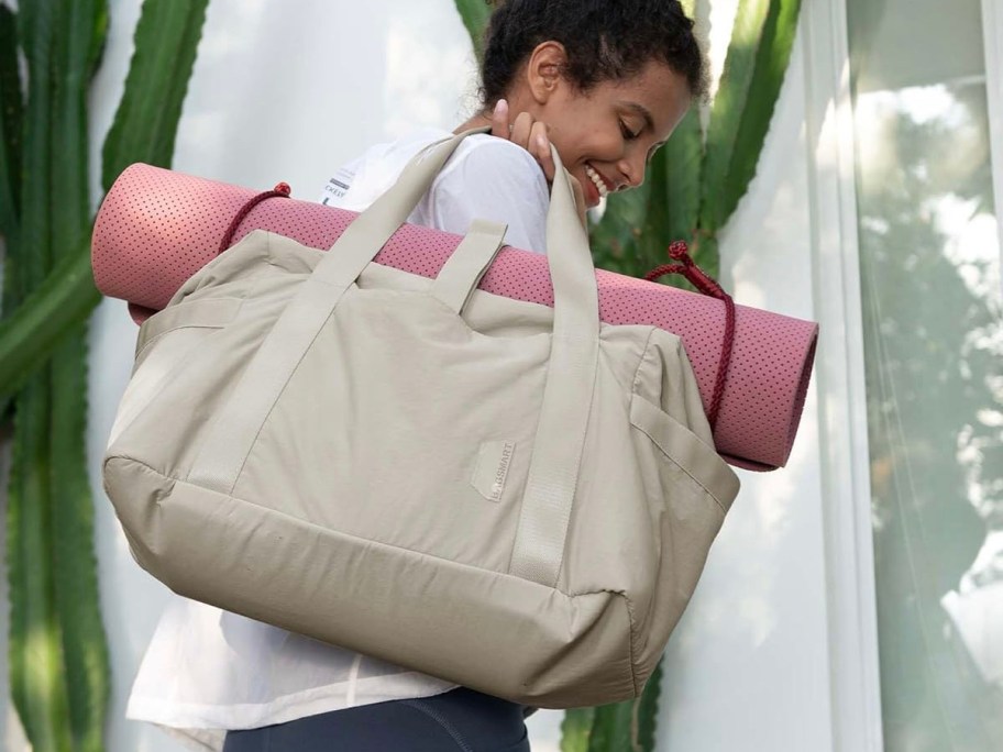 woman holding beige travel bag with pink mat rolled on top