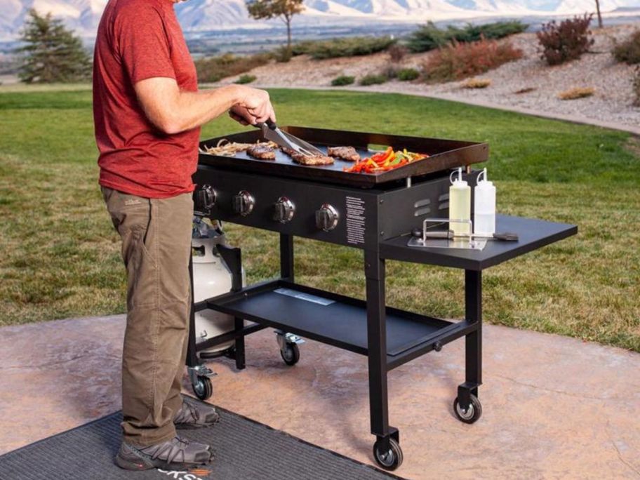 man grilling on Blackstone 4 Burner Liquid Propane Outdoor Griddle in Black