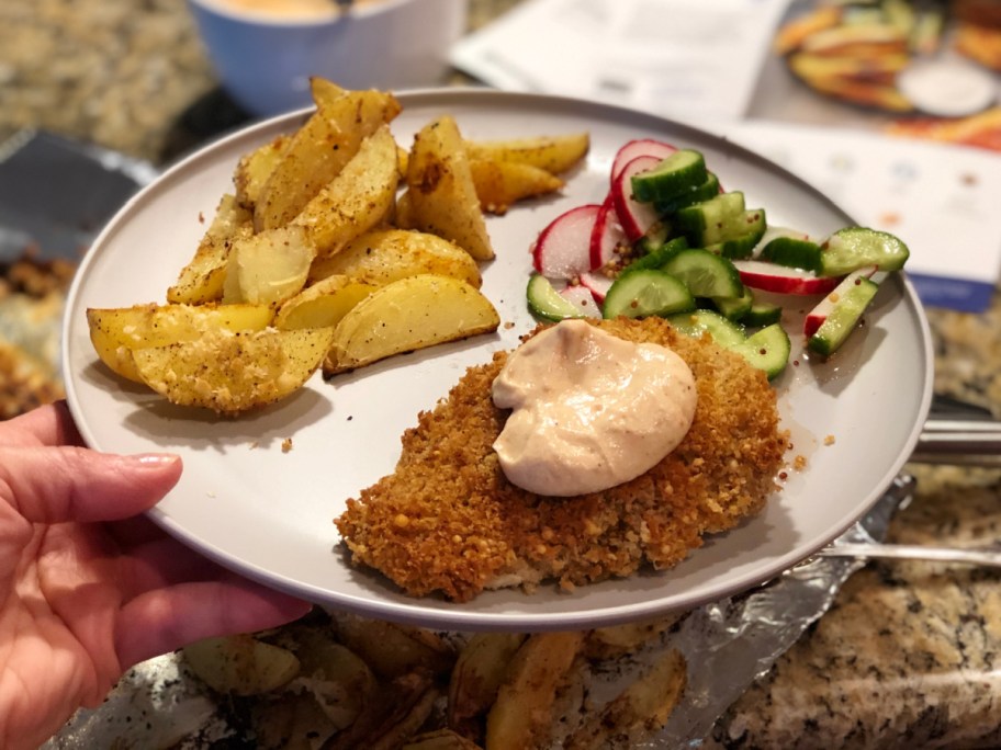 hand holding plate of chicken potatoes and greens