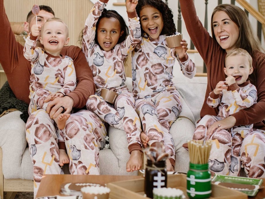 family celebrating with arms in the air sitting on a couch wearing matching football themed pajamas