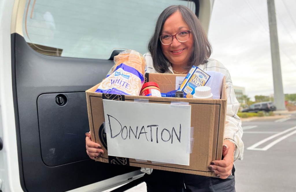 smiling woman holding a box of donation items in front of an open vehicle door