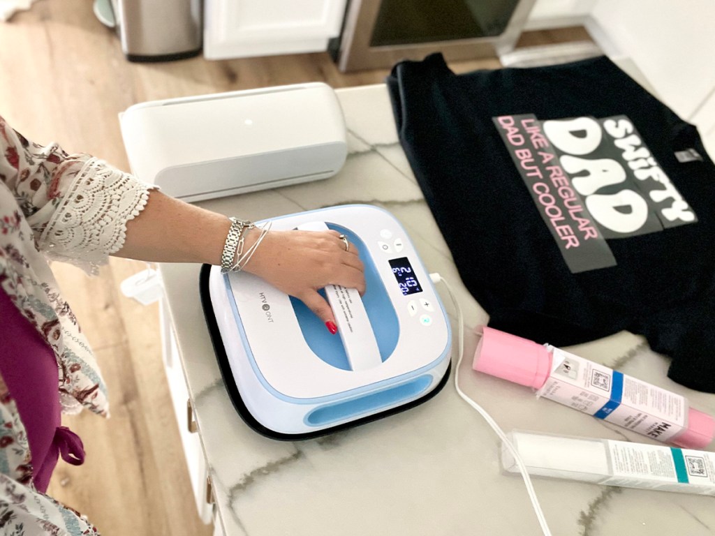 woman holding heatpress on table with shirt and materials