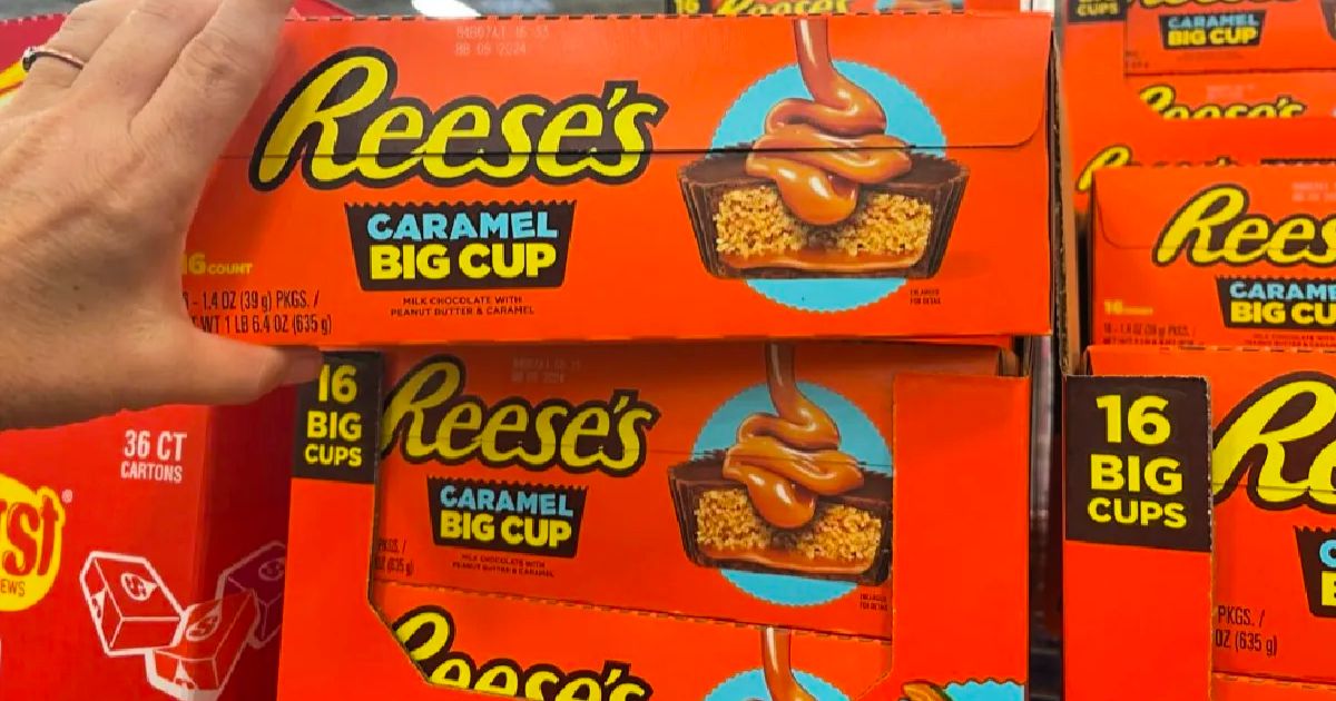 a womans hand grabbing a box of reeses caramel big cups off a shelf