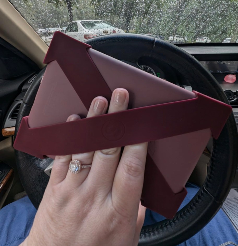 hand holding back of silicone stray on kindle on car steering wheel with rainy on windshield 