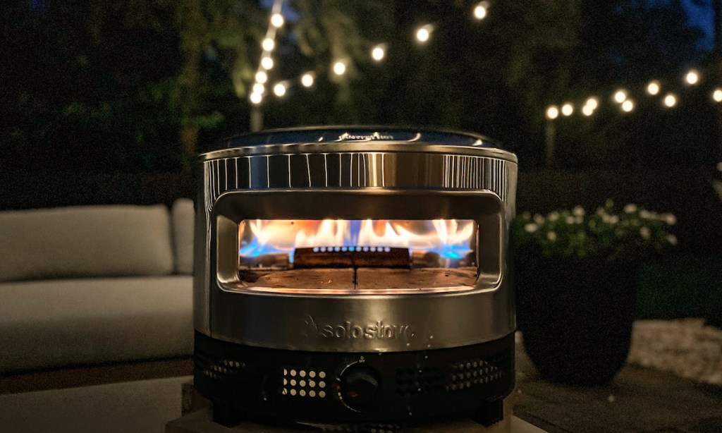 solo stove pizza oven with flame outside in dark with string lights