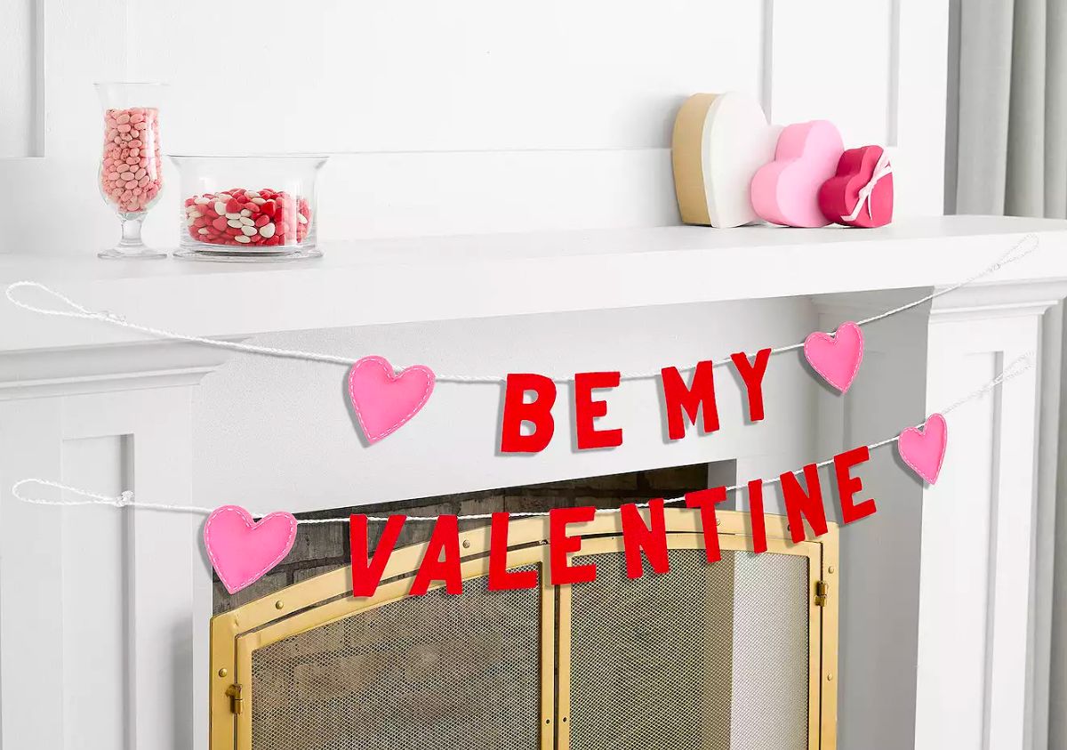 a garland strung across a fireplace mantle in the words be my valentine