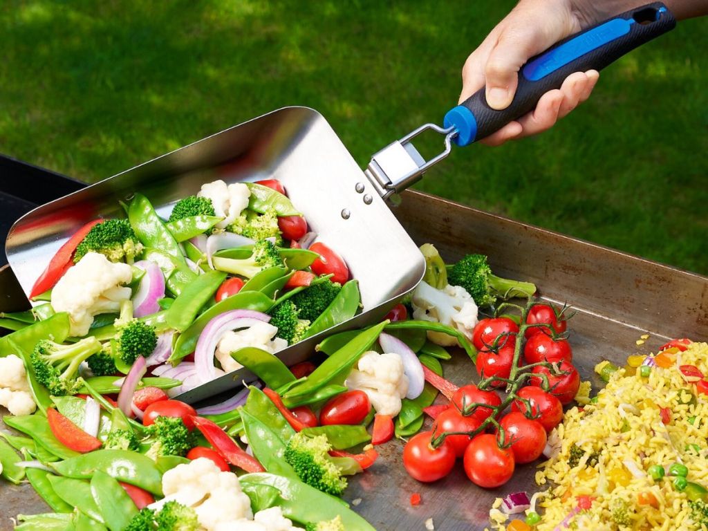 Hand scooping veggies on a griddle using a Mr BBQ super scooper