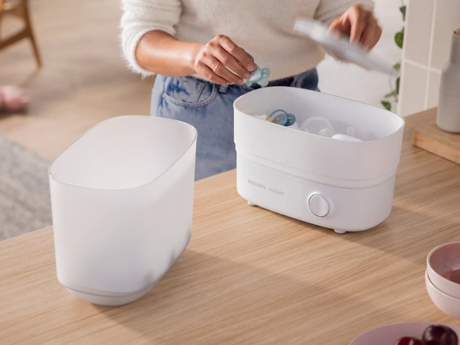 woman placing baby body in a white and grey baby bottle sterilizer