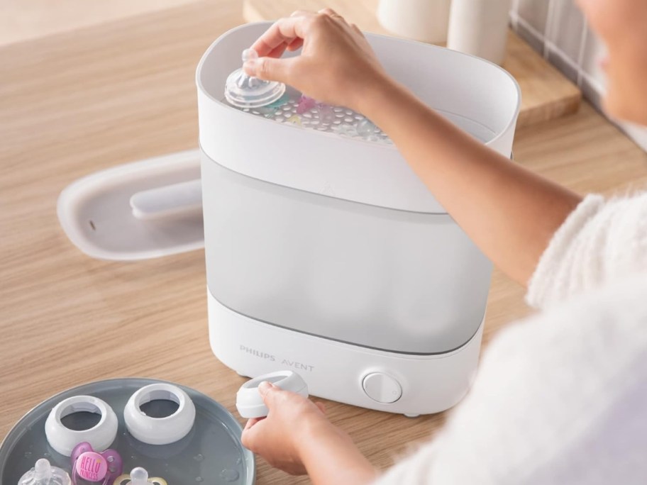 woman placing baby body in a white and grey baby bottle sterilizer