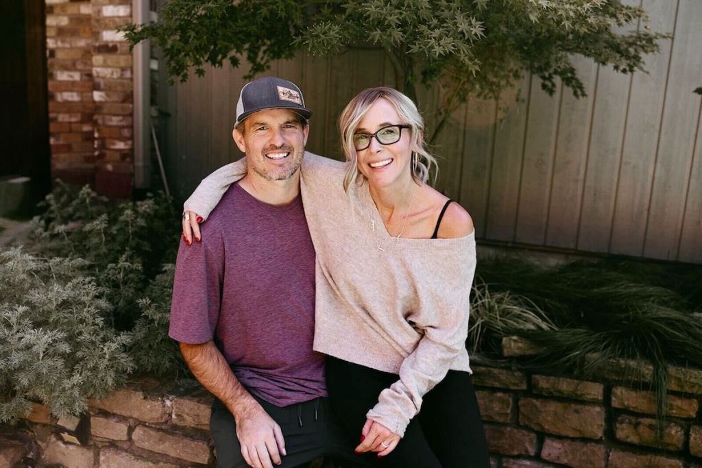 couple sitting with arms around each other sitting on ledge in front of house