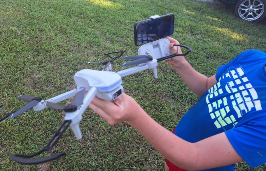 boy in blue shirt holding a drone with remote standing in grass